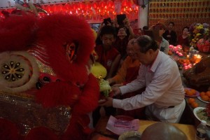 古晋佛教居士林在大年初一也邀请舞狮队前来贺节。图为蔡明田林长及释学闻法师从舞狮口中接过彩青是影。